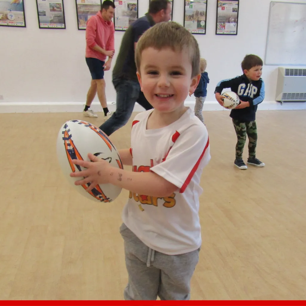 A young child holding a rugby ball during a Rugby Stars session